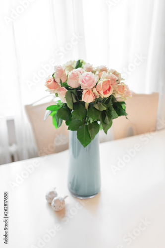 Bouquet of peach colored roses in light blue vase on table.