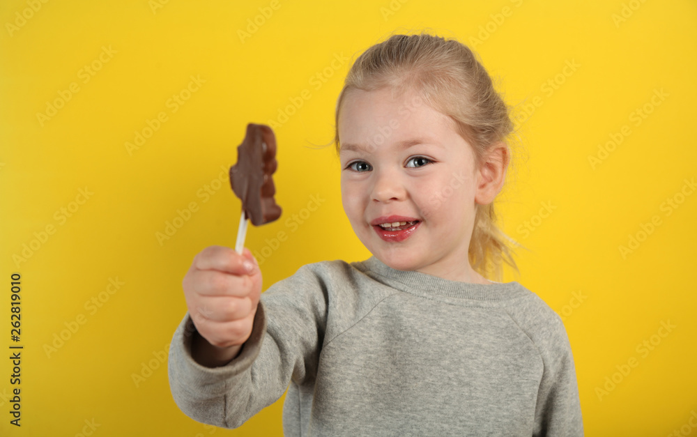 Cute girl child eating sweet chocolate candy on yellow background. Happy childhood. Cute girl child eating sweet chocolate candy on yellow background. Happy childhood.