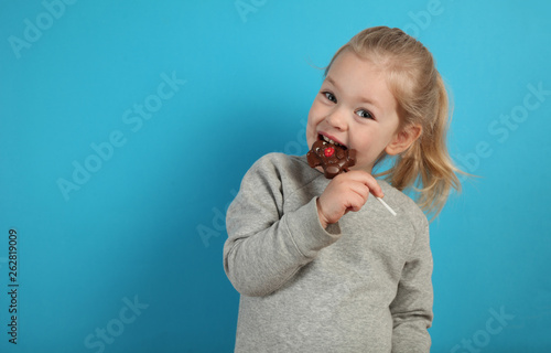 Cute girl child eating sweet chocolate candy on blue background. Happy childhood.