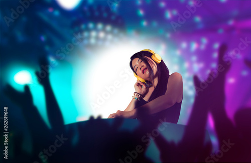 young attractive and happy Asian Korean DJ woman remixing using deejay gear and headphones at night club with lights background in clubbing fun and music concept