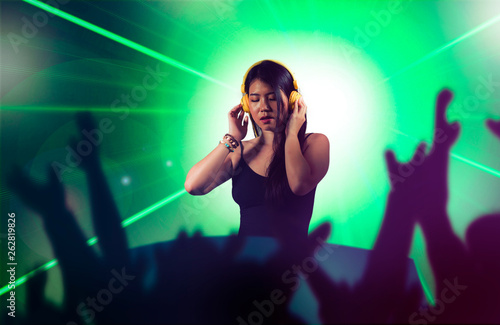 young attractive and happy Asian Korean DJ woman remixing using deejay gear and headphones at night club with lights background in clubbing fun and music concept