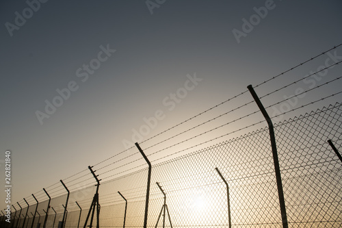 Metal security fence located in front of cloudless sky with bright sun photo