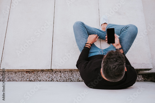 Middle age handsome elegant happy male in casual wear using a mobile phone and sitting near grey wall photo