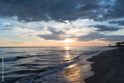 Sunset on the beach with a cloudy sky  calm sea and islands in the background