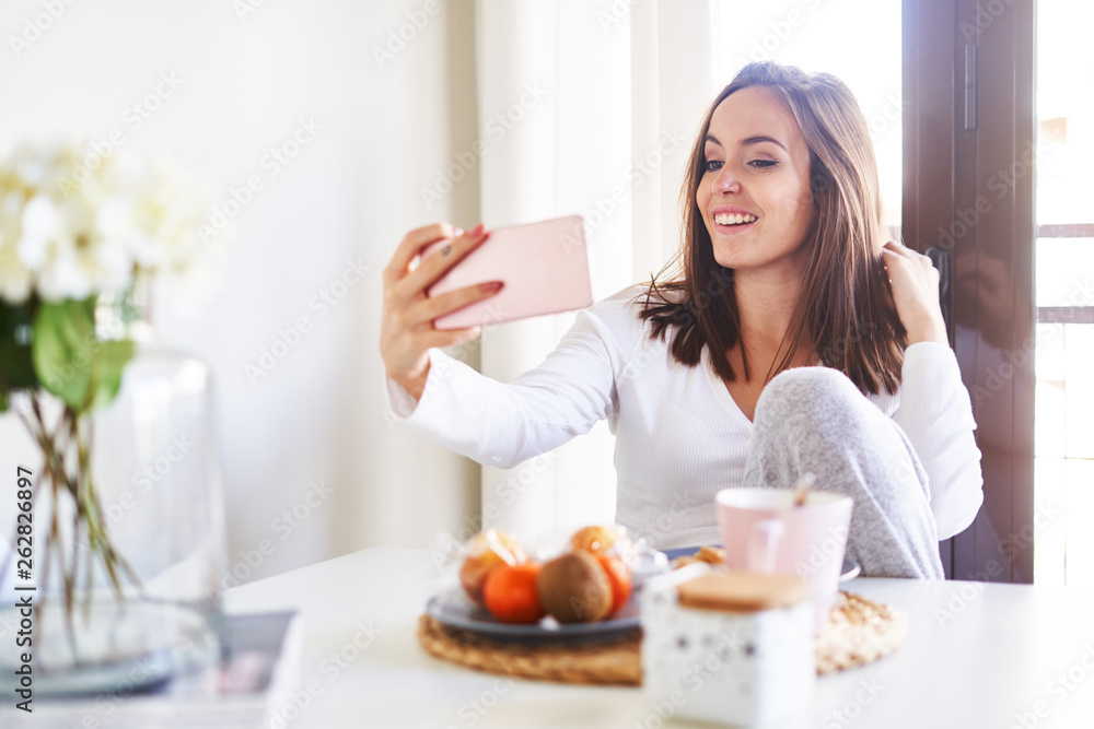 Attractive young happy woman having fun and taking selfie on mobile phone near window at home Attractive young happy woman having fun and taking selfie on mobile phone near window at home
