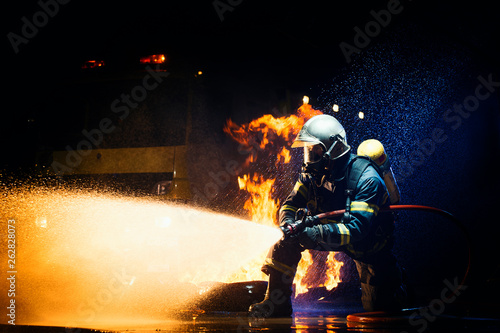 Unrecognizable male in firefighter uniform suppressing fire with heavy stream of water photo