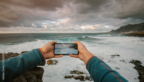 First person view of a man taking a picture with phone at a seashore landscape