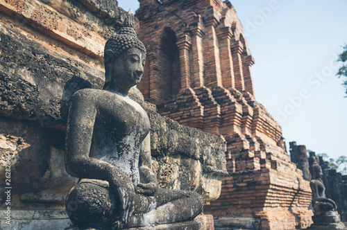 Weathered statue of Buddha located near shabby stone walls of ancient oriental temple in Thailand photo