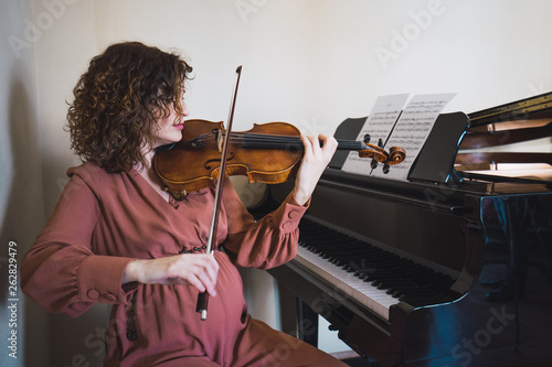 Woman sitting next to a piano playing a violin photo