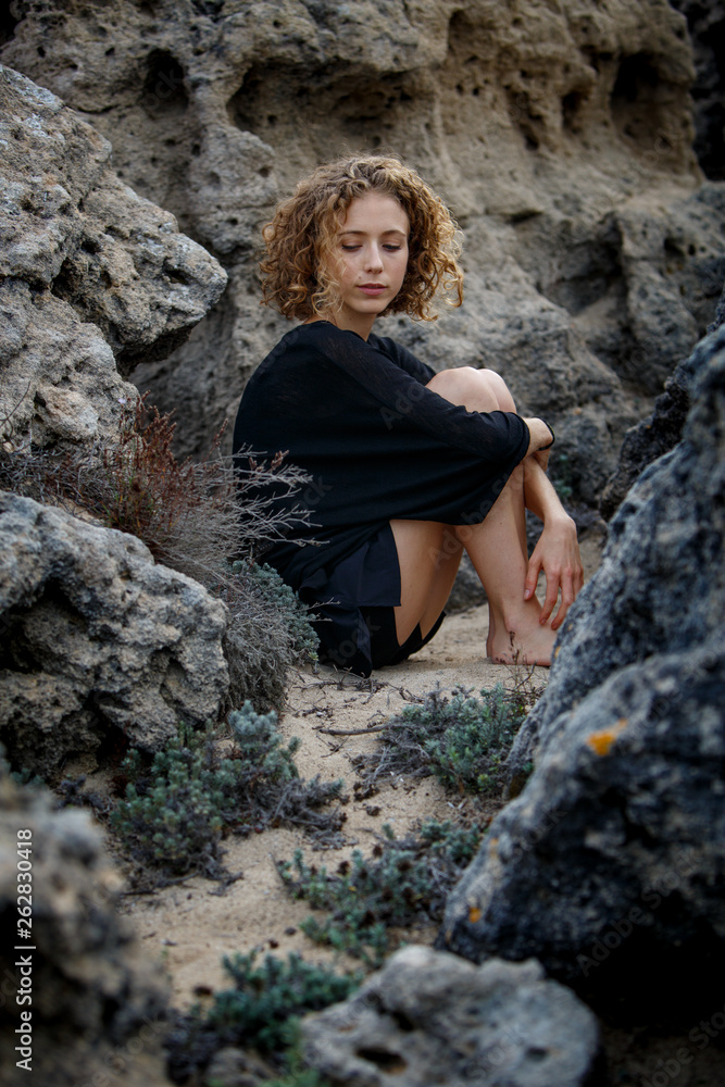 Young attractive charming woman sitting between rocks Young attractive charming woman sitting between rocks