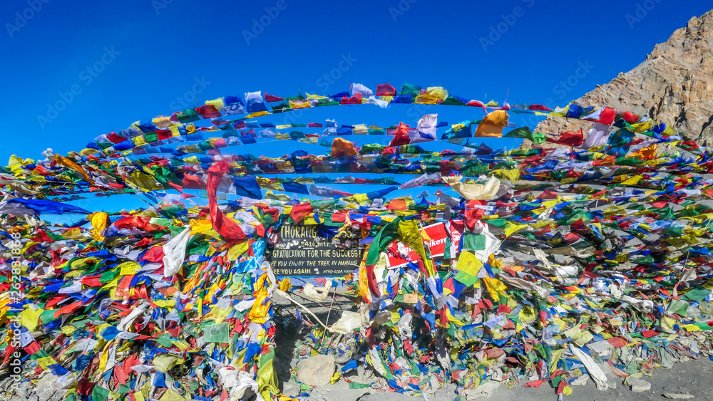 The waving flags at the top of Thorung La Pass, Annapurna Circuit Trek, Nepal. Congratulations for the effort. Colorful Prayer flags attached to the stone wall, blow by the wind. Clear sky.