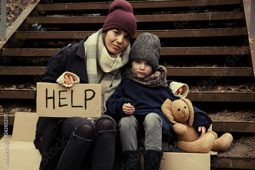 Bild auf Leinwand Poor mother and daughter with HELP sign sitting on stairs outdoors