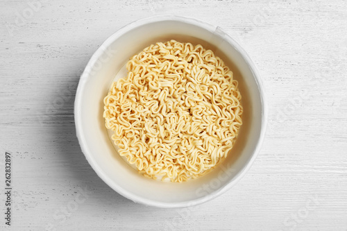 Cup of instant noodles on white wooden background, top view