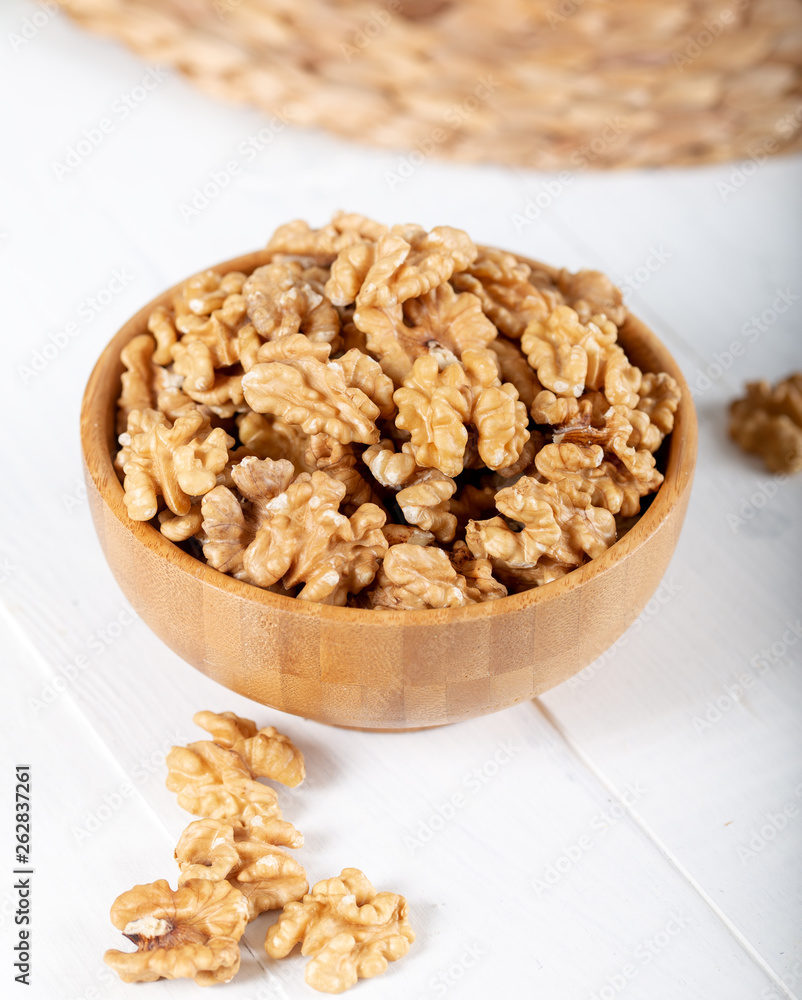 Walnut kernels in a wooden bowl on white background.