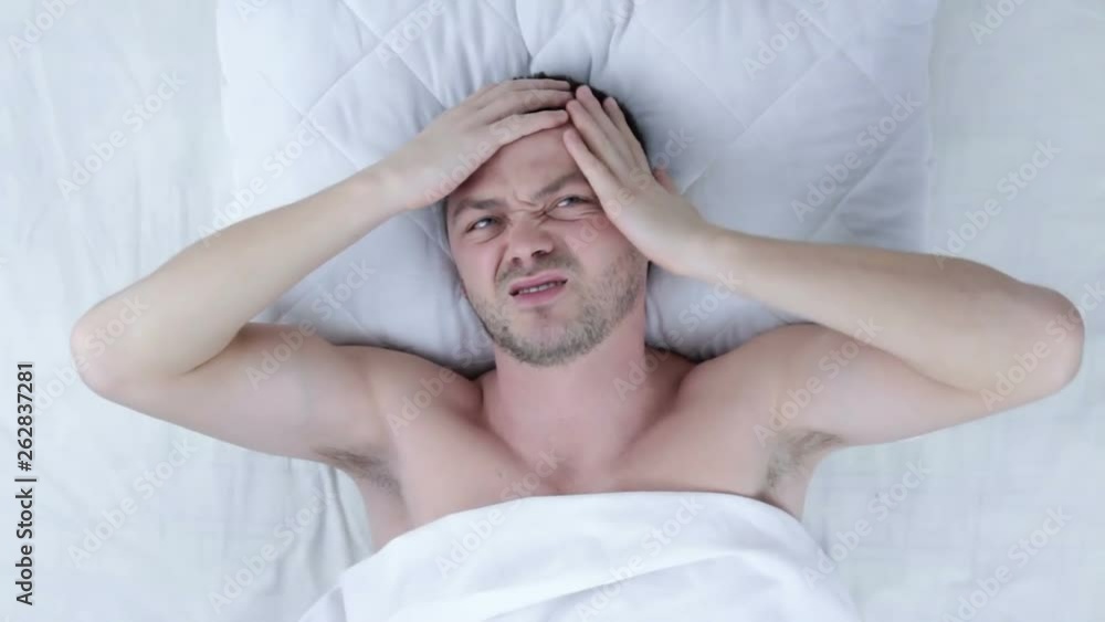Man with headache waking up in bed at home - sleeping and people concept Man with headache waking up in bed at home - sleeping and people concept