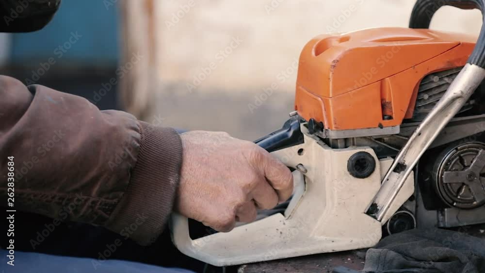 grandfather repairs a chainsaw,an old man repairs a chainsaw in his yard in the village grandfather repairs a chainsaw,an old man repairs a chainsaw in his yard in the village