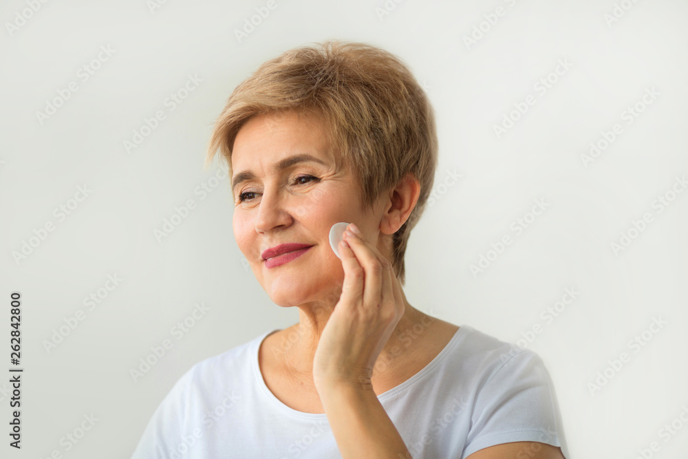 stylish beautiful elderly woman with a short haircut on a white background cleans face stylish beautiful elderly woman with a short haircut on a white background cleans face