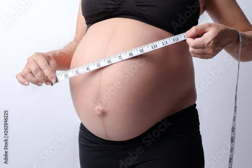 Pregnant women wear black shirts. who measured her stomach with a tape measure on a white background