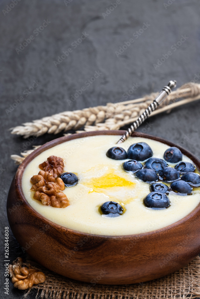 Wooden bowl of semolina porridge with blueberry and walnut on black stone background Wooden bowl of semolina porridge with blueberry and walnut on black stone background