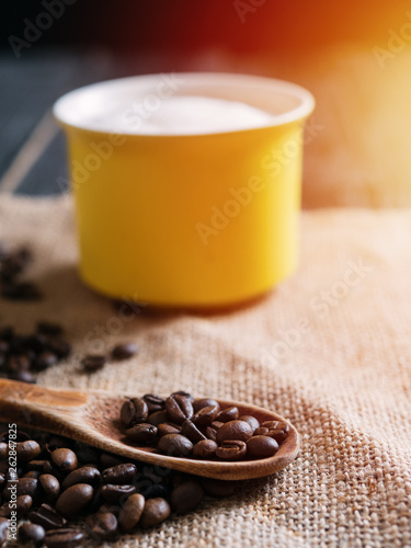Yellow cappuccino coffee mug and coffee beans in wooden spoon