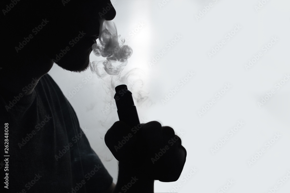 male vapor silhouette exhales a cloud of smoke using an electronic cigarette . copy space