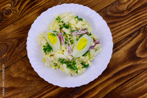 Salad with chinese cabbage, onion, sausage, eggs and mayonnaise on wooden table