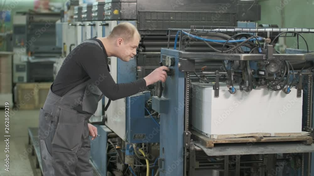 Man working on the printing press machine checks the paper supply to the printing press Man working on the printing press machine checks the paper supply to the printing press