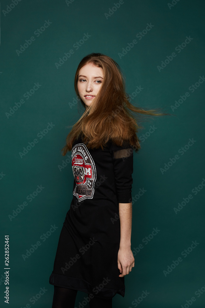 Stylish and beautiful young model girl in black fashionable dress and boots isolated over dark-green background in studio Stylish and beautiful young model girl in black fashionable dress and boots isolated over dark-green background in studio