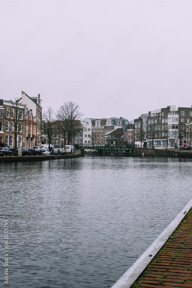 Obraz premium Beautiful cityscape in Haarlem, Netherlands. Tiny waves on the river, bridge, and dark bricked houses on the both sides of the canal. Cold cloudy weather.