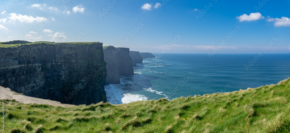 Fototapeta Panoramiczny widok na szereg irlandzkich klifów z zieloną trawą na pierwszym planie
