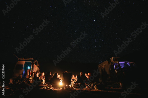 Campfire with lots of people and camper van at night.