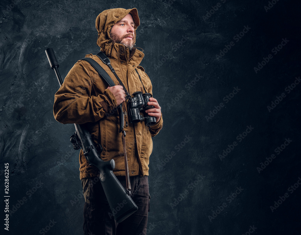 Hunter with shotgun holding binoculars and looking sideways. Studio photo against dark wall background