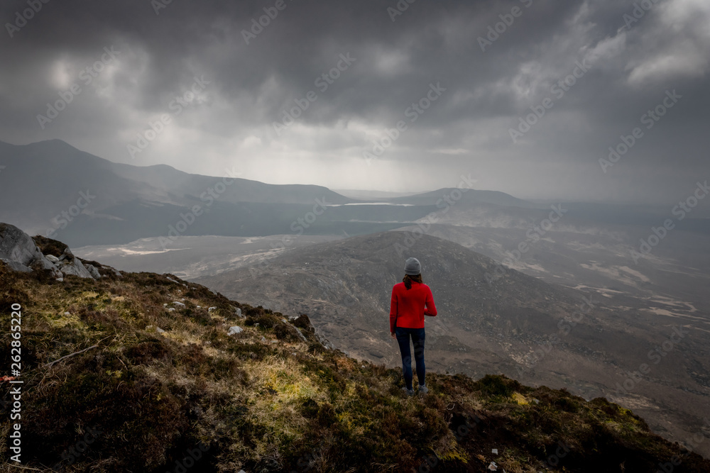 une femme en haut d'une montagne devant un paysage grandioses  sous un ciel menaçant