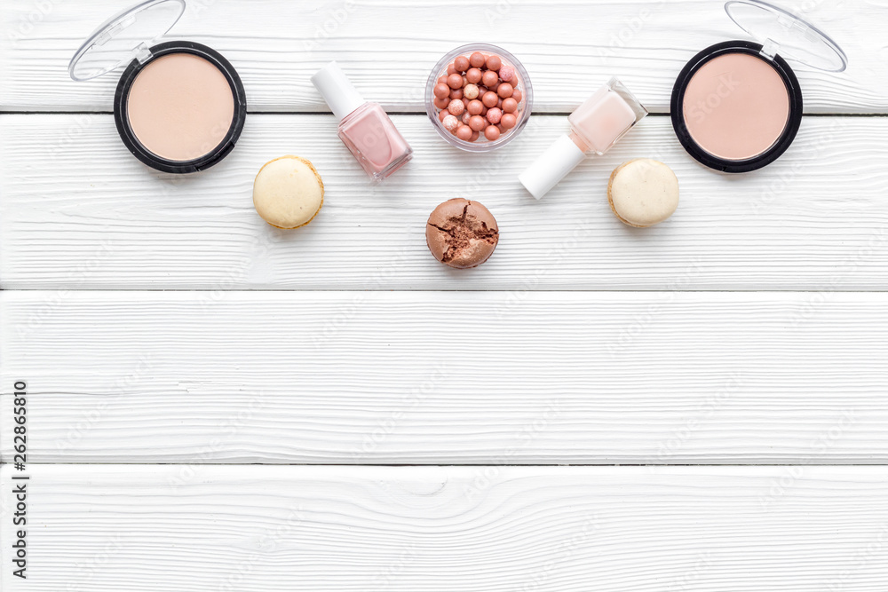 Make-up artist desk with powder, decorative cosmetics and macaroon cookies on white wooden background top view mokeup Make-up artist desk with powder, decorative cosmetics and macaroon cookies on white wooden background top view mokeup