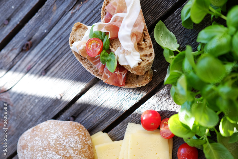 Small sandwiches with meat, cherry tomatoes, cheese, bread and basil on the black table.