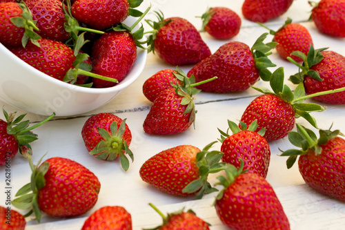 Fresh strawberries in ceramic bowl on white wooden background.