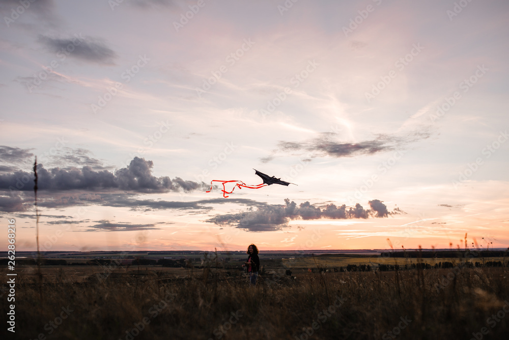 A young girl launches a kite into the sky in a field at sunset