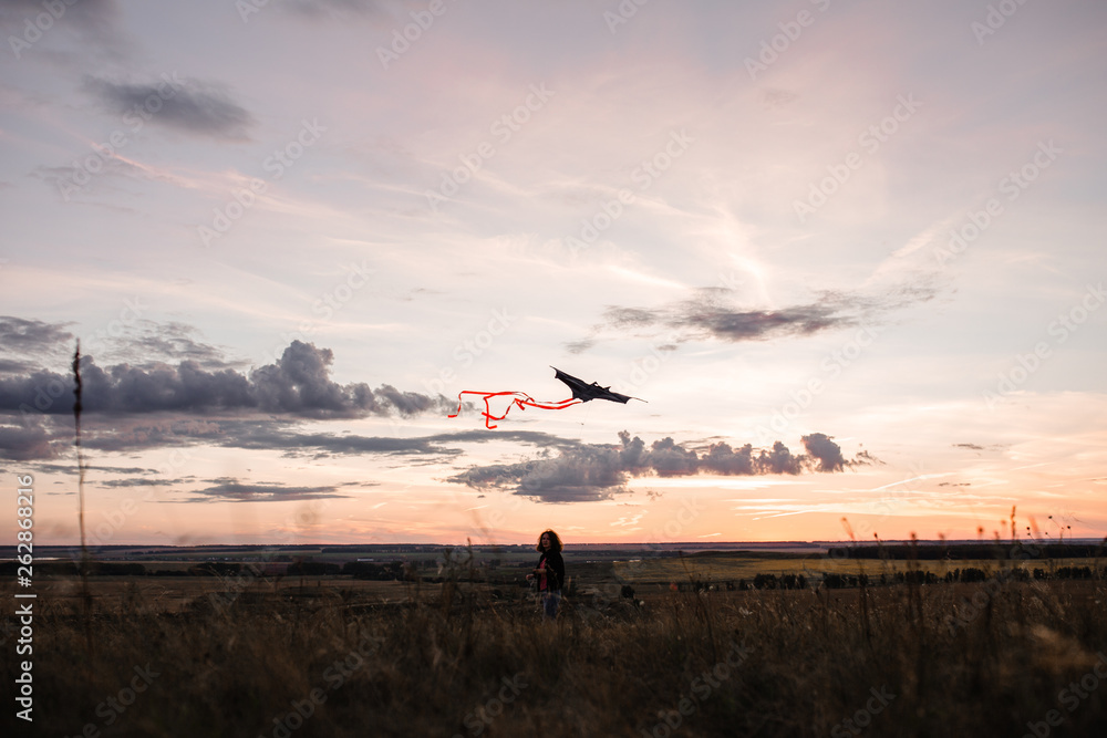 A young girl launches a kite into the sky in a field at sunset A young girl launches a kite into the sky in a field at sunset