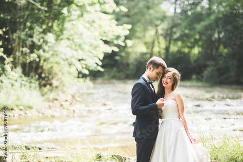 Beautifull wedding couple kissing and embracing near the shore of a mountain river with stones