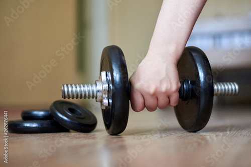The hand of the girl takes a dumbbell from the floor at home, home sports, healthy lifestyle