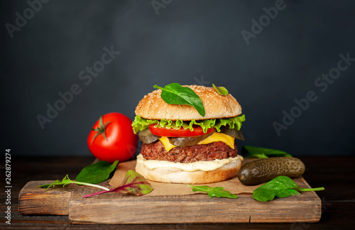 Homemade hamburger with lettuce, tomato, cheese and cucumber on a cutting board
