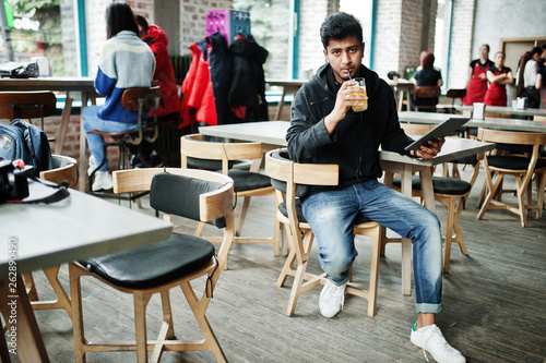 Casual and stylish young asian man with earphones at cafe drinking juice from glass and holding tablet.