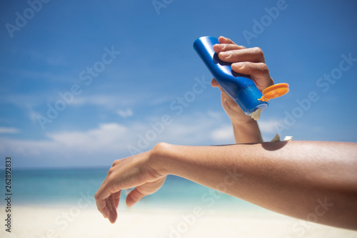 Woman applying sunscreen on her hands from a bottle on the beach with the sea in the background. SPF sunblock protection concept.selective focus photo