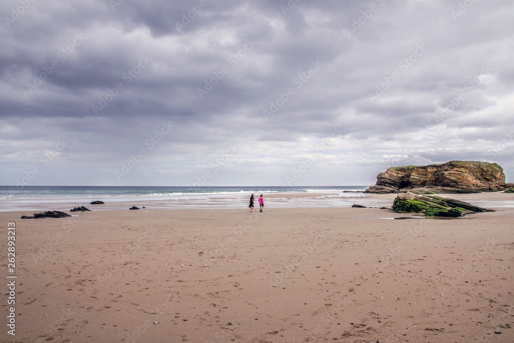 Dos personas pasean por la playa en un dia nublado