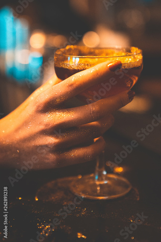 Golden cocktail glass at the bar. Young women's hand holding a martini glass with a golden stardust on top of it. photo