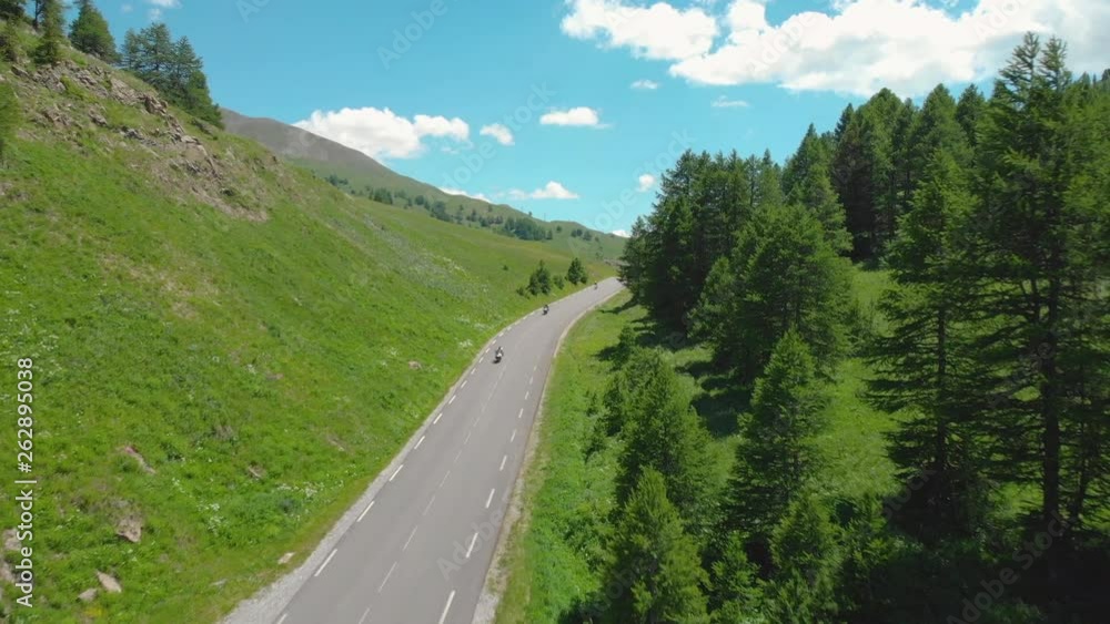 AERIAL: Motorbike riders and white car drive along the mountain road in the tranquil French Alps on a sunny spring day. Tourists enjoy the scenic road trip through the breathtaking green valley. AERIAL: Motorbike riders and white car drive along the mountain road in the tranquil French Alps on a sunny spring day. Tourists enjoy the scenic road trip through the breathtaking green valley.