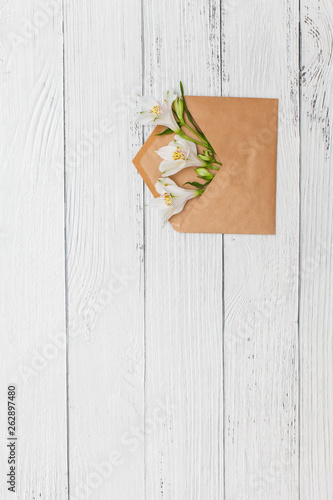 Flat lay with White lilies in craft envelope on old white wooden background.