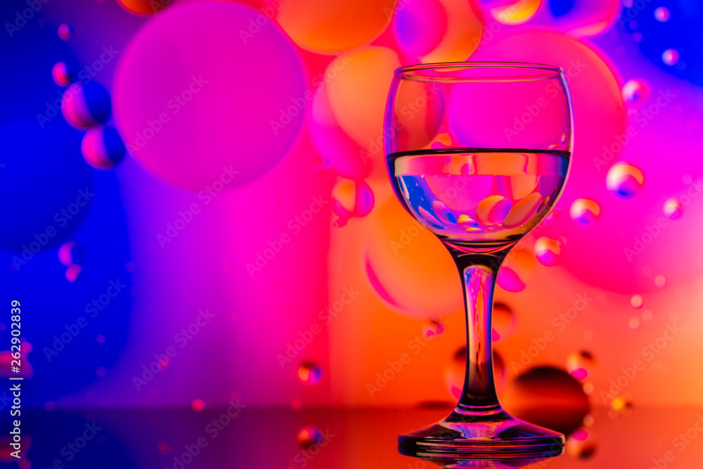 transparent glasses with water and oily drops on colorful background transparent glasses with water and oily drops on colorful background