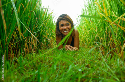 natural and fresh portrait of young happy and exotic islander Asian girl from Indonesia smiling cheerful and excited posing in green field playing with rice enjoying holidays