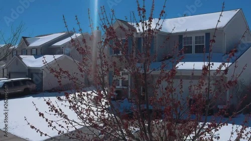 Spring Transition Drone Shots from inside a snowy suburban neighborhood, with a tree with bright red buds in shot. photo